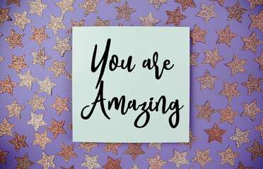 You are Amazing text  motivational and inspiration quote on paper card with star glitter decoration flat lay on purple background