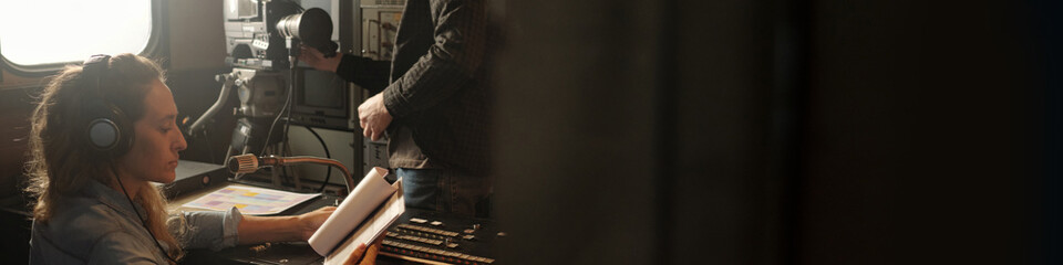 Header of woman in headphones looking through text in paper documents while sitting by sound mixing...