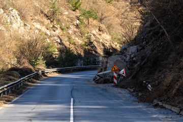 Rockslide blocking mountain road with warning signs indicating danger