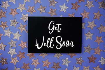Get Well Soon text on paper card with star glitter decoration flat lay on purple background