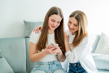 Beautiful mother hugs her teenage daughter and looks at the phone together. Emotional relationship of child and mom. Mother's Day. Greetings on the holiday.