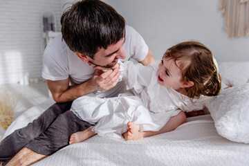 Father and daughter sharing a joyful moment on a cozy bed, capturing the essence of family love and...
