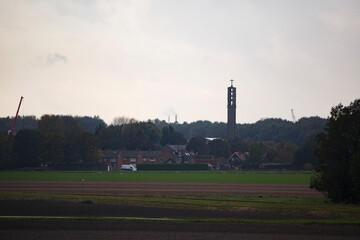 Obraz premium View of a countryside village with a church tower and smoke stacks on a cloudy day