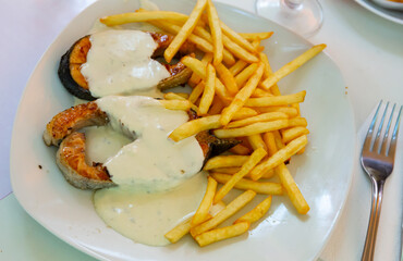 Dish of tasty fried salmon with white sauce and french fries potatoes on plate