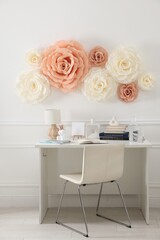 Beautiful decorative paper flowers on white wall and stylish furniture indoors