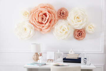 Beautiful decorative paper flowers on white wall above desk indoors