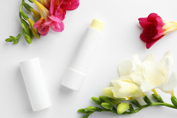 Lip balm and freesia flowers on white background, flat lay