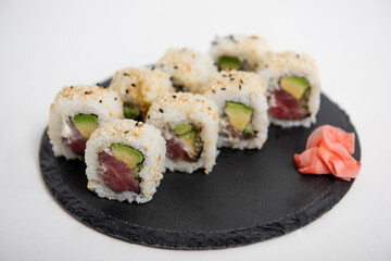 Close-up of sushi California rolls with tuna, avocado, and sesame seeds, served on a black slate plate against a white isolated background