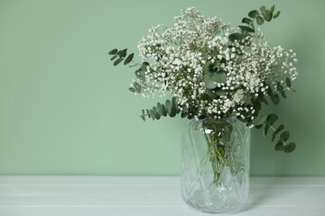 Beautiful gypsophila flowers and eucalyptus branches in vase on white table against turquoise...