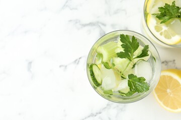 Healthy drink with parsley, cucumbers, lemon and celery on white marble table, flat lay. Space for text
