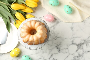 Delicious bundt cake, Easter eggs and tulips on white marble table, flat lay. Space for text