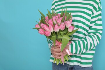 Woman with bouquet of beautiful tulips on light blue background, closeup. Space for text
