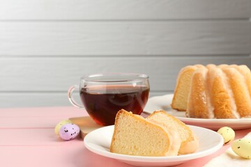 Pieces of delicious bundt cake, Easter eggs and tea on pink wooden table