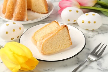 Pieces of delicious bundt cake, Easter eggs and tulips on light marble table, closeup