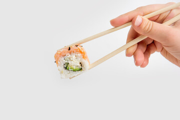 Hand holding a fresh sushi Philadelphia roll with chopsticks against a white background. The roll...