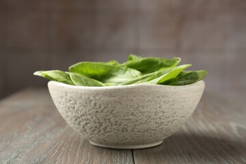 Fresh green sorrel leaves in bowl on wooden table, closeup