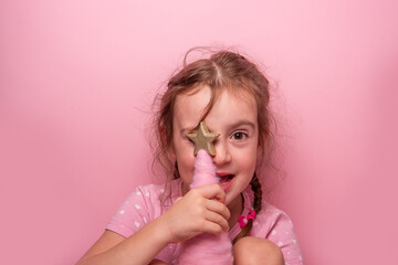 Close up portrait of cheerful young girl with braided hair holding golden star decoration against...