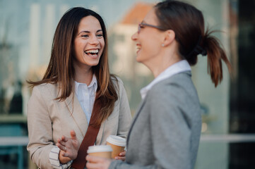 Two businesswomen laughing together during coffee break outdoors