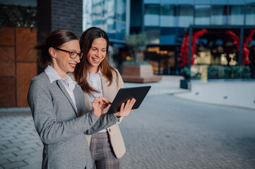 Two businesswomen using digital tablet outside office building