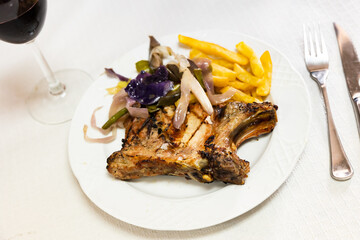 Pork loin tenderloin chop with cooked vegetables and fries on a white plate. Serving a delicious Spanish dish Chuleta de cerdo with potatoes