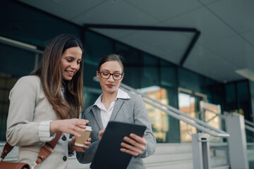 Businesswomen using tablet and drinking coffee outside office building