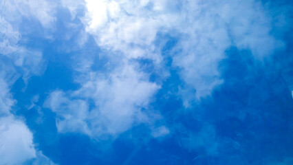 水中の中から波や波紋で歪んだ水面に映る青い空と雲を見上げた抽象的な風景