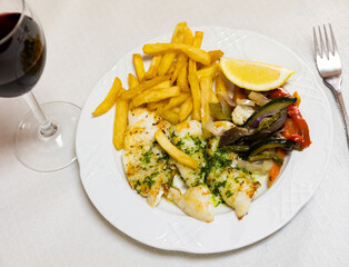 Delicious pink fish grilled with French fries and stewed vegetables. Fish with vegetables and a slice of lemon on a plate top view