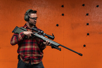 A male sniper holds a rifle with an optical sight in his hands at a shooting range.