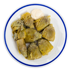 Plate is filled with baked vegetables topped with garlic sauce. Cooked artichoke cores with white hot sauce made from olive oil, garlic, egg yolks and lemon juice. Isolated over white background