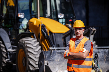 Construction worker stands confidently in front of a yellow excavator on a bright sunny day at a...
