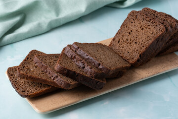 Slices of dark rye bread arranged neatly on a wooden platter against a soft green background