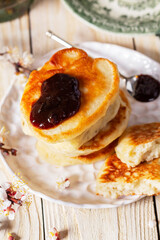 Lenten yeast pancakes with plum jam and tea, and a bouquet of flowering apricot branches on a light wooden table.