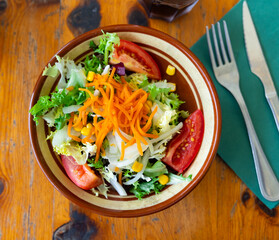 Plate contains portion of salad from fresh China cabbage, grated carrot, corn, tomato complemented by small glass of wine.