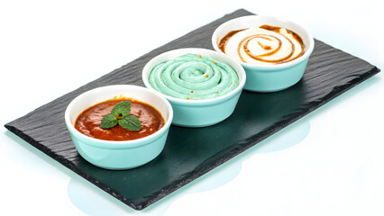 Artfully arranged trio of colorful dipping sauces served in small bowls on slate platter, evoking sense of culinary delight and creativity