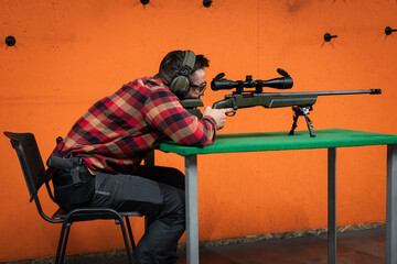 A civil shooter aims a sniper rifle from a sitting position at a shooting range.
