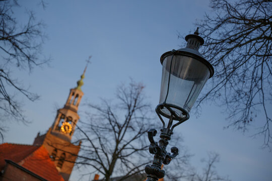 Historic street lamp illuminated with soft evening light near an old church in a serene town square during twilight hours