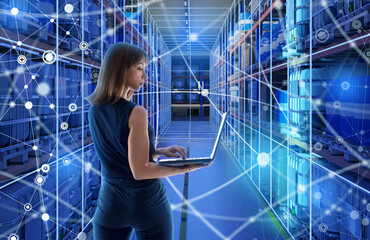 Woman using a laptop in a high-tech warehouse surrounded by digital network overlays, representing...