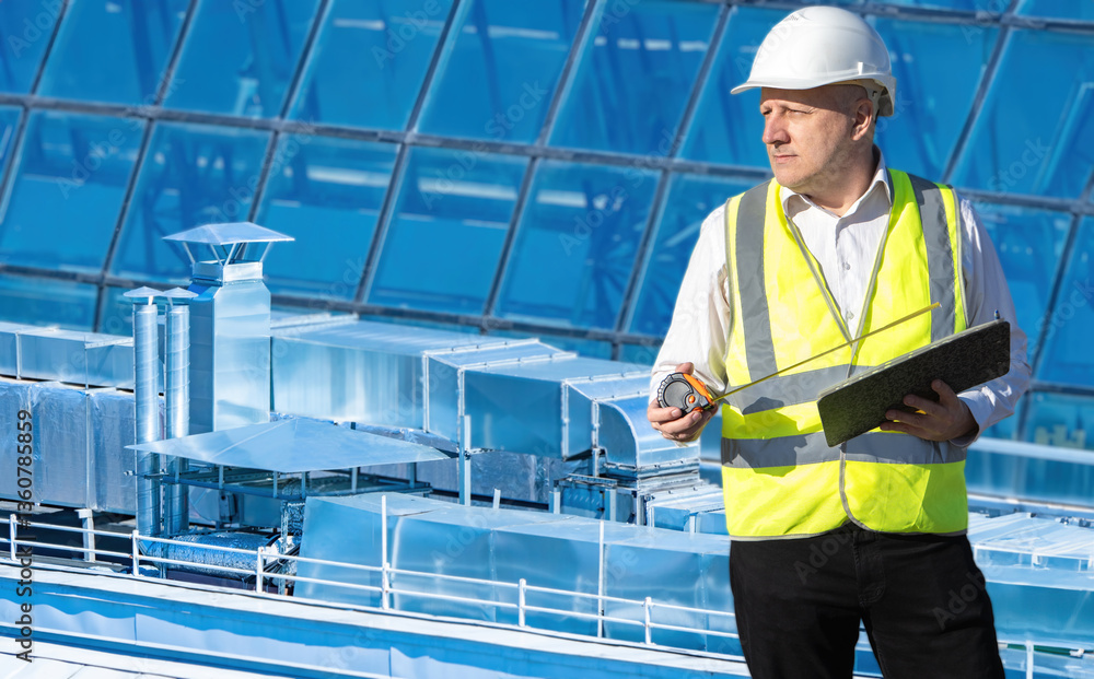 Poster man engineer sets up ventilation system. worker with tape measure on roof. ventilation pipes behind 