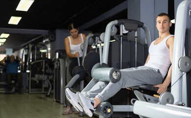 Young athletic man in sportswear training her legs on machine in gym