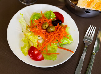Salad of seasonal vegetables is prepared on plate. ingredients are served in large chunks, Chinese cabbage, tomatoes, grated carrots, olives - vitamin snack or aperitif