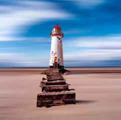 An old white lighthouse with a red roof on a sandy beach with the sea and sky in the background