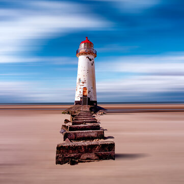An old white lighthouse with a red roof on a sandy beach with the sea and sky in the background