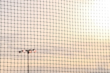 Sun Over Mesh Fence and Stadium Lights