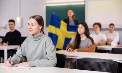Young students study in classroom, teacher stands behind with Swedish flag