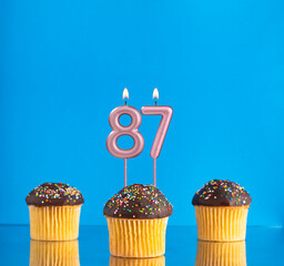 Birthday candle with the number 87 - Three cupcakes on a blue background.