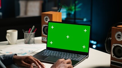 African american man working from home with green screen on laptop, looking at data on the web. Remote worker in personal apartment office crosschecking important info. Camera B.