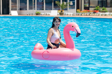 Pool party. Positive happy woman float at swimming pool in pink flamingo, festival, vacation, hotel, beach, event smiling, during summer, copy space. spa resort advertisement