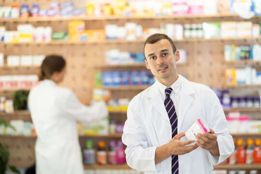 Smiling young man chemist demonstrating medicament in box in pharmacy store
