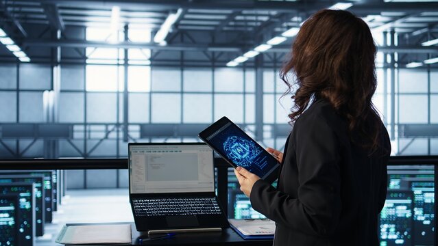 Technician in data center with tablet integrating AI driven automation tools, running predictive maintenance routines. Woman ensuring continuous uptime of server room, managing data flows, camera B