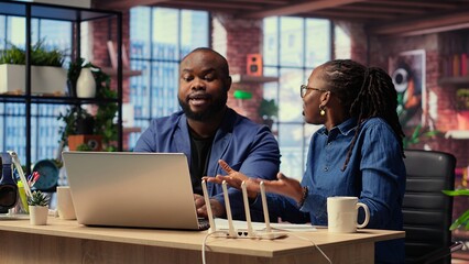 Fototapeta premium Angry African American people tries to reset the Wi Fi modem due to signal loss, woman arguing and being irritated. Frustrated couple fighting over troubleshooting methods. Camera B.